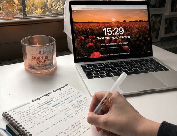 A laptop and a girl writing by the window