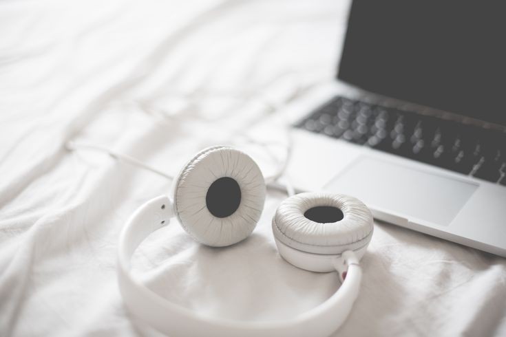 A white headphone and a laptop to listen to the podcast