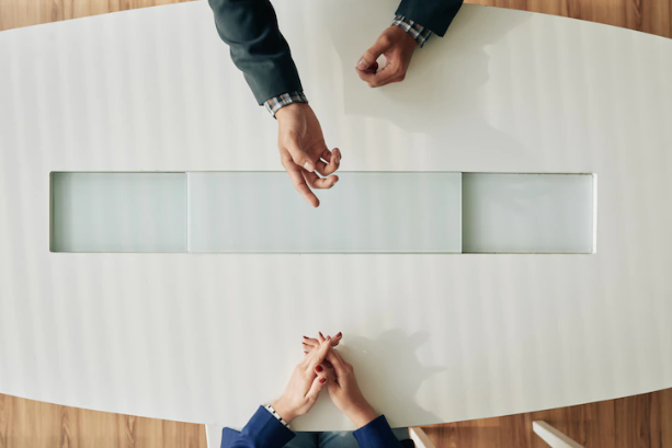 A table is shown from above showing the hands of two people speaking