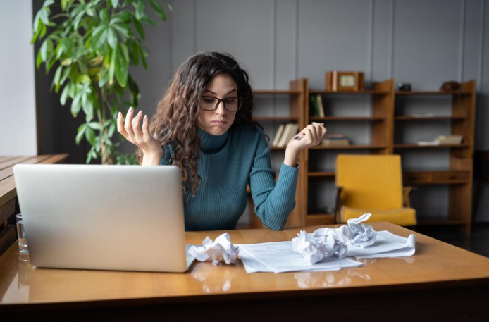 A girl has several crumpled papers and a laptop next to it