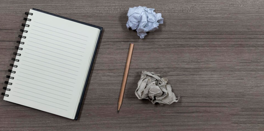 A pencil and notebook with some crumpled paper