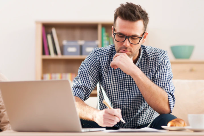 A man who has a laptop and is writing on paper