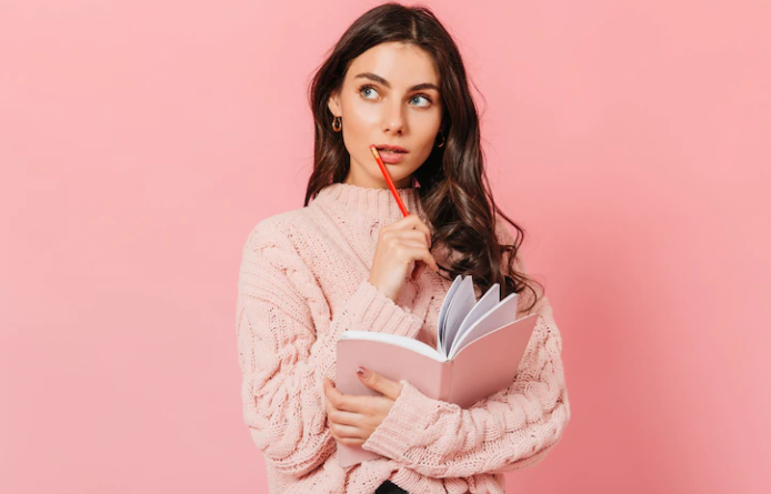 A girl who is thinking and holding a book and a pencil