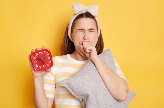 A girl holding a watch and a pillow and yawning