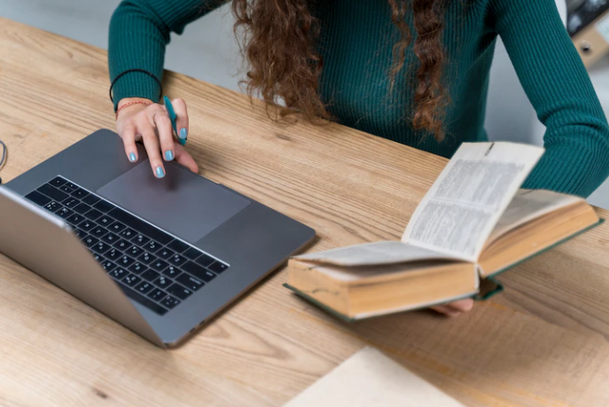 A girl is holding a book and searching on a laptop