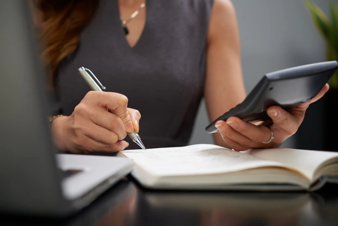 A girl is working with a calculator and writing in the notebook